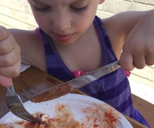 Kid-friendly summer eats in Brooklyn: kid cutting pizza slice with fork and knife
